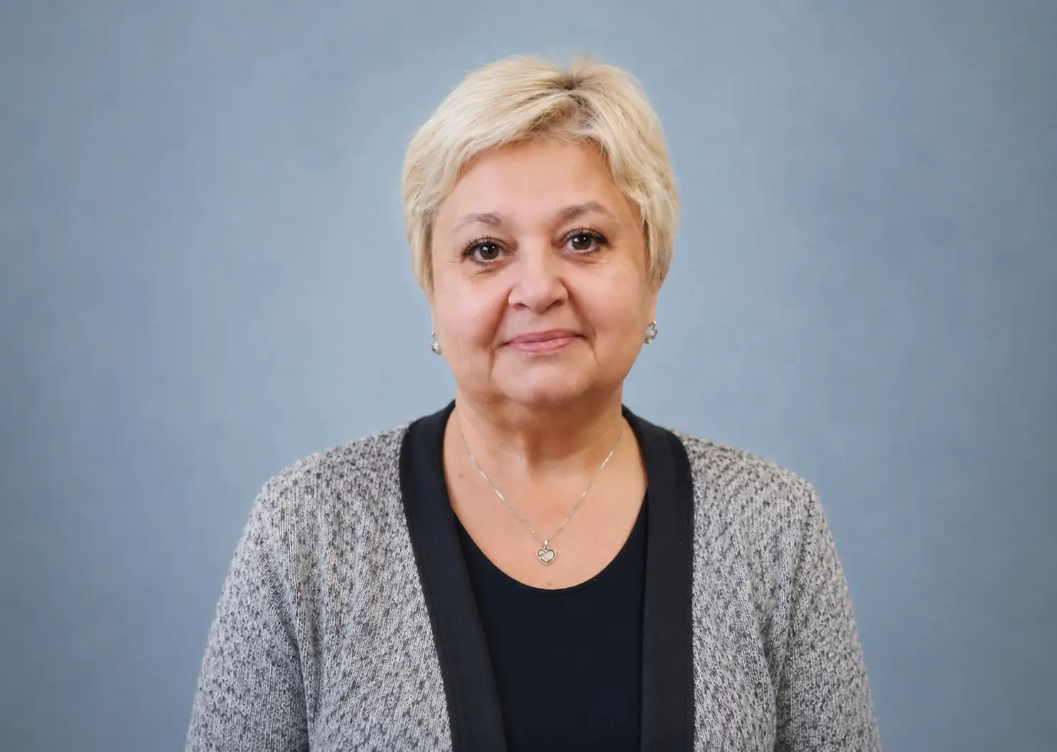 Poradkyně s krátkými blond vlasy v šedém svetru na modrém pozadí